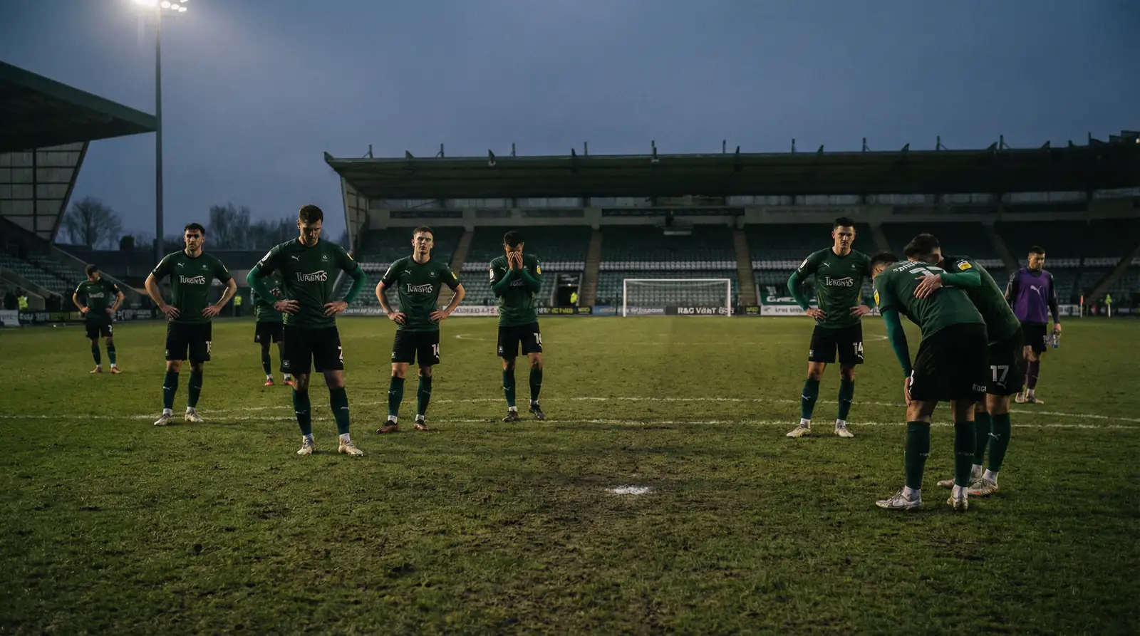 Imreoirí sacair i ngeansaithe glasa tar éis cluiche pionóis, mothúcháin díomá ar a n-aghaidheanna