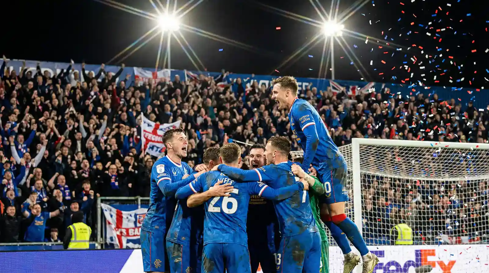 Foireann sacair idirnáisiúnta ag ceiliúradh cúil ar pháirc mhór le bratach náisiúnta